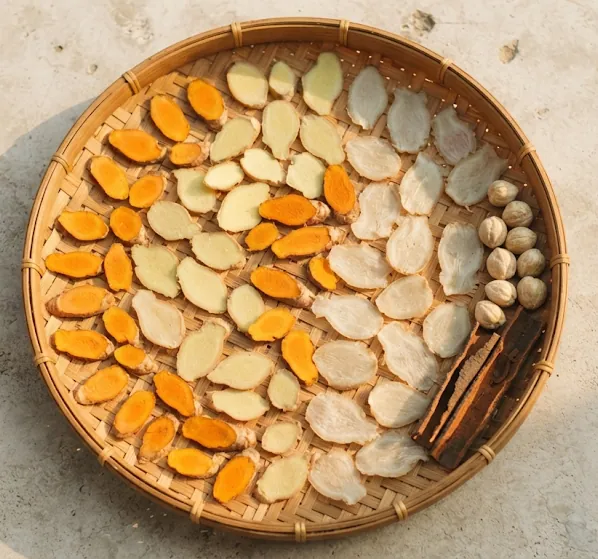 Sliced turmeric, ginger and galangal drying on a woven bamboo tray